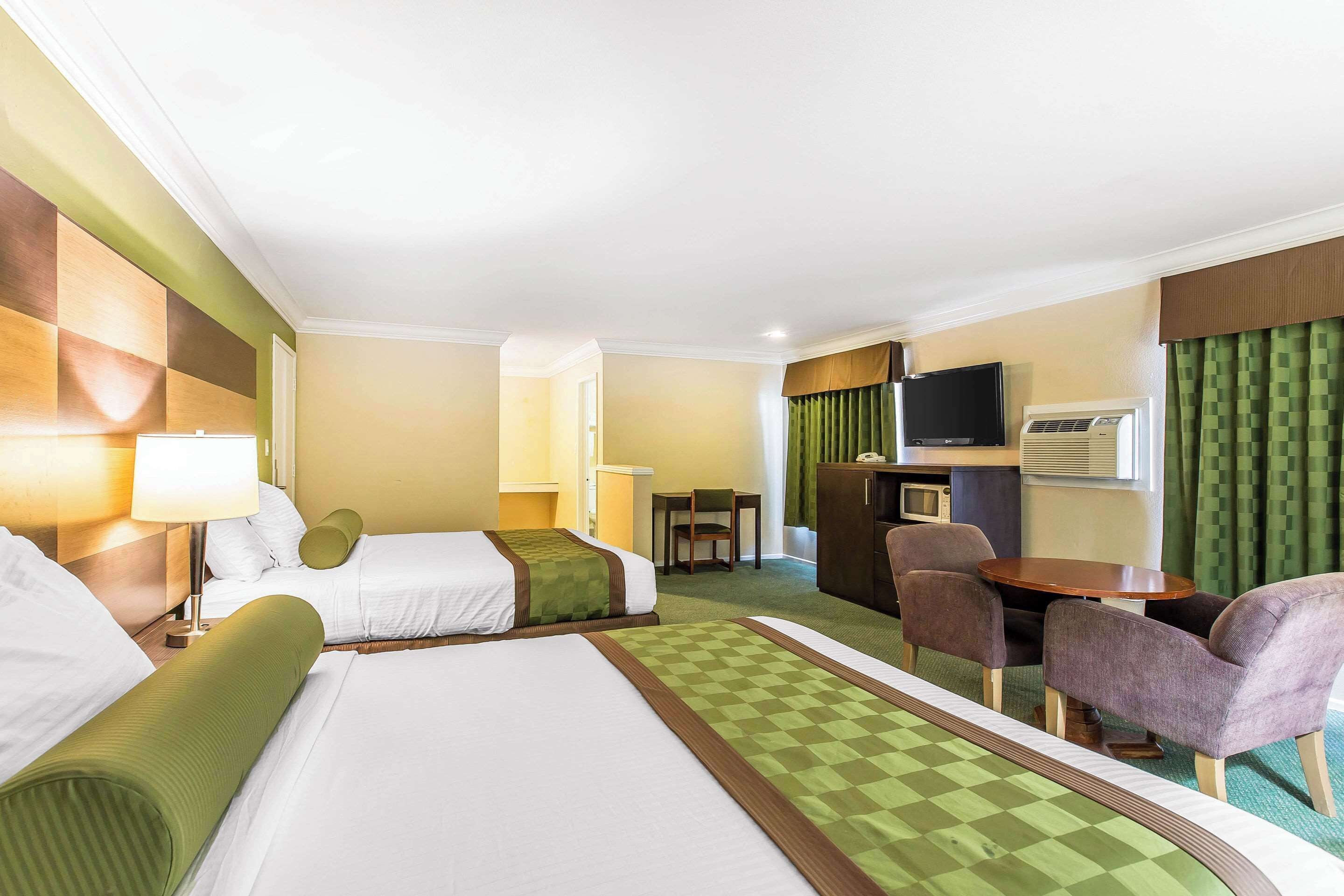A hotel room with two beds, a desk, a chair, a television, and an air conditioning unit.