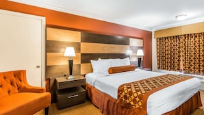A hotel room with a large bed, a nightstand, a chair, and a headboard with a checkered pattern. - Rodeway Inn & Suites Canyon Lake-Menifee West (Menifee)