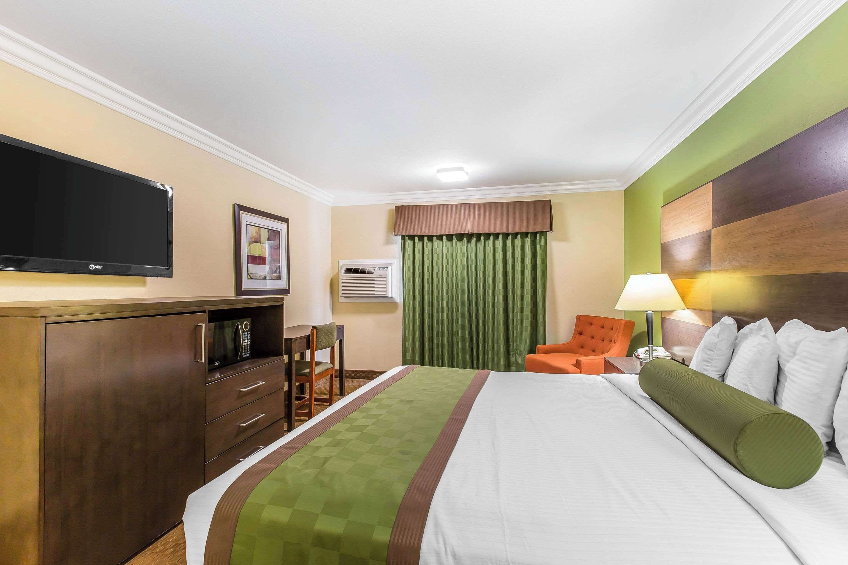 A hotel room with a bed, a desk with a chair, a television, and a window with curtains.