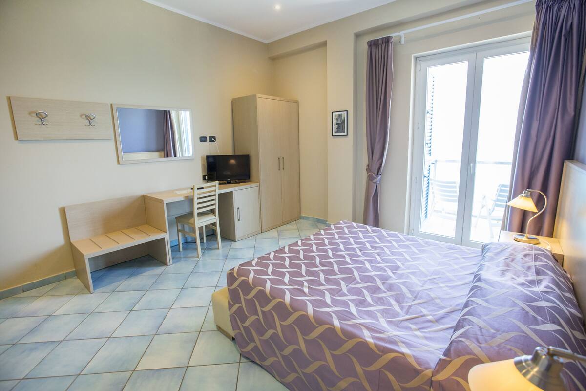 A hotel room with a bed, a desk, a television, and a wardrobe.