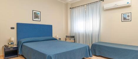 Een hotelkamer met twee bedden, een nachtkastje, een lamp, een airconditioning en een raam met gordijnen.
