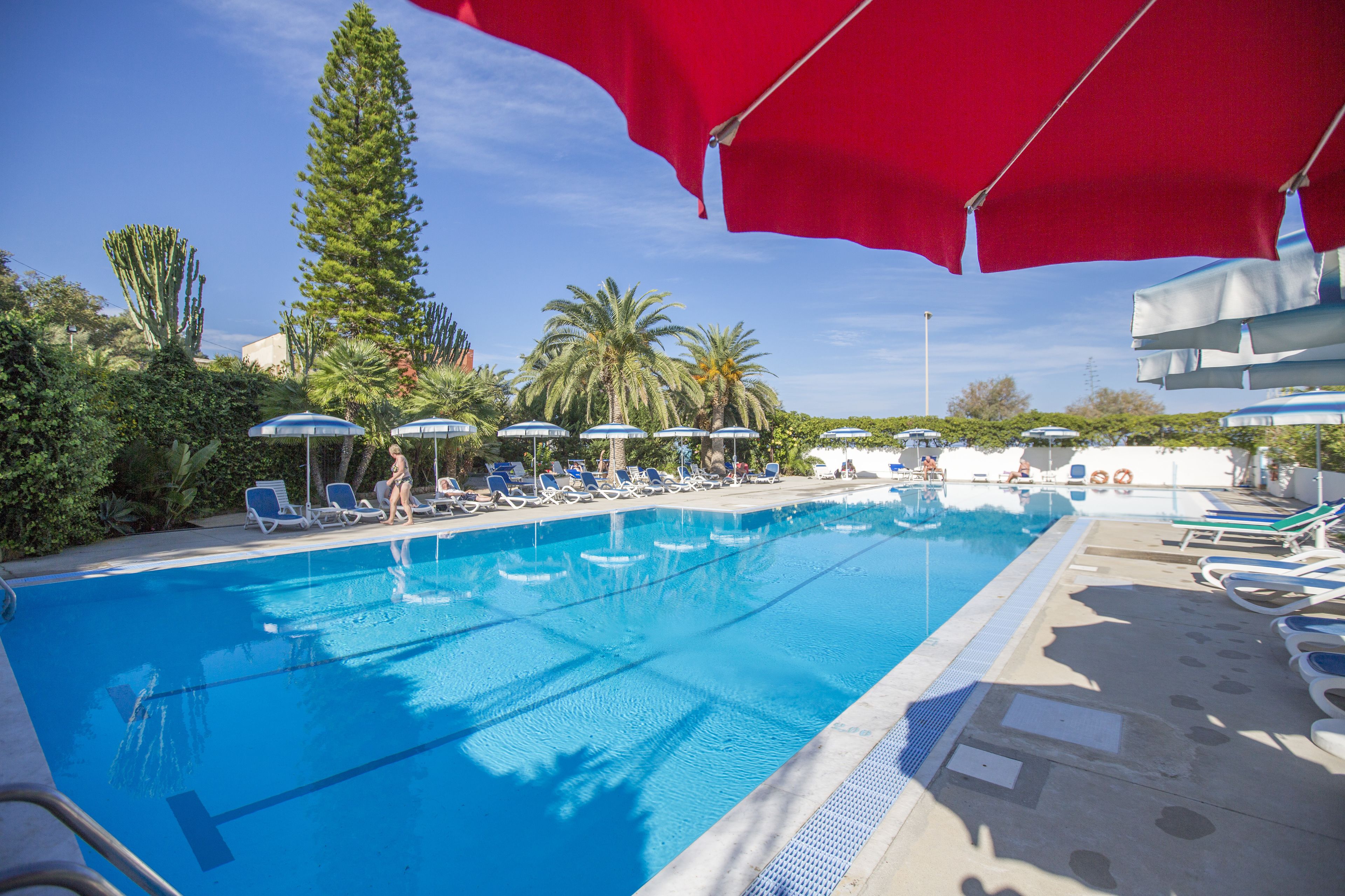 A swimming pool with blue water, surrounded by lounge chairs and umbrellas.