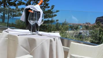 Mesa dispuesta con una botella de champán, dos copas de vino y cubiertos, con vistas a un paisaje costero.