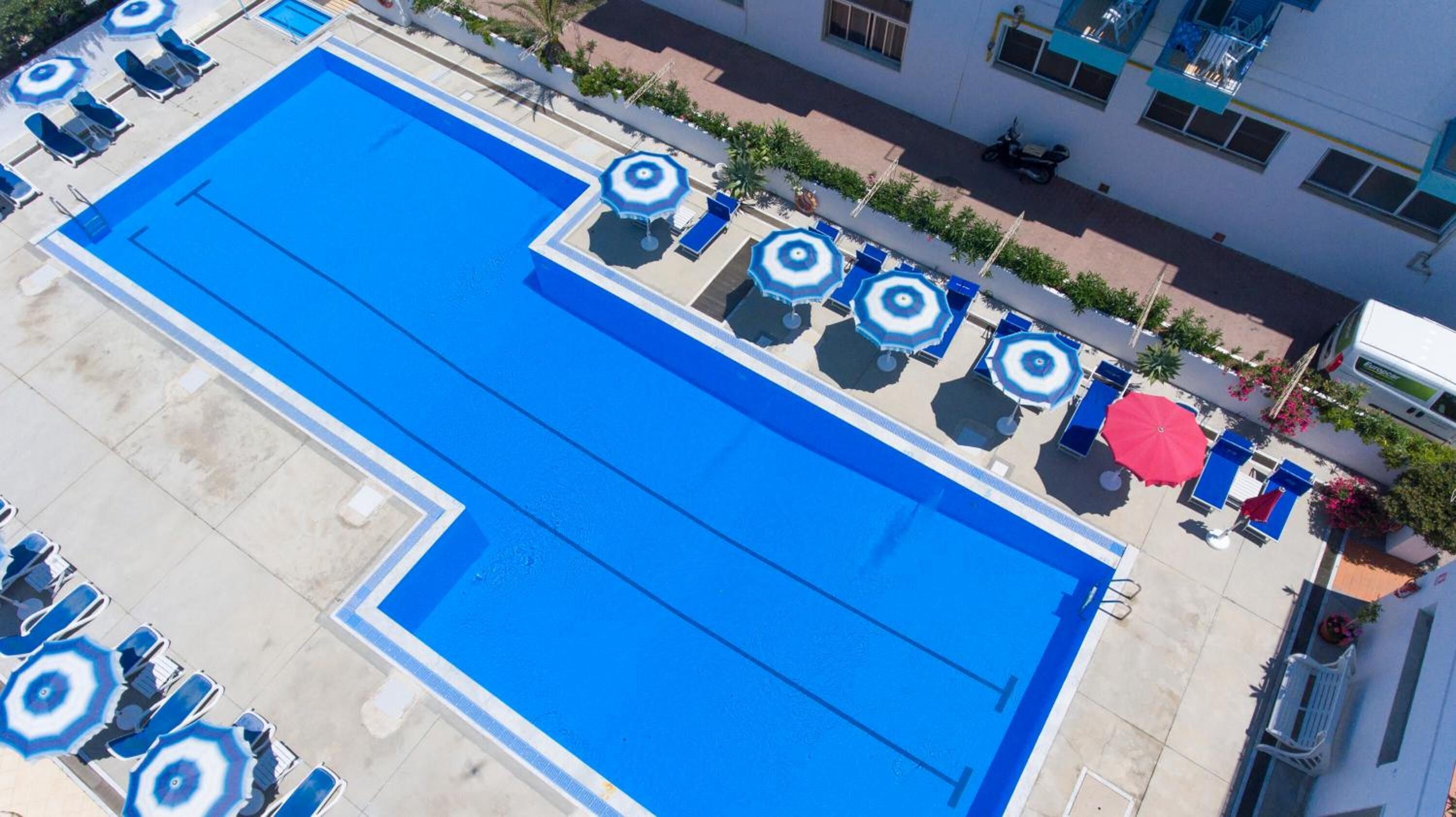 Una piscina en la azotea con varios sillones de sol y sombrillas, rodeada por un edificio con balcones.