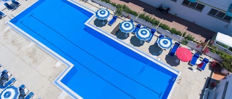 Una piscina en la azotea con varios sillones de sol y sombrillas, rodeada por un edificio con balcones.