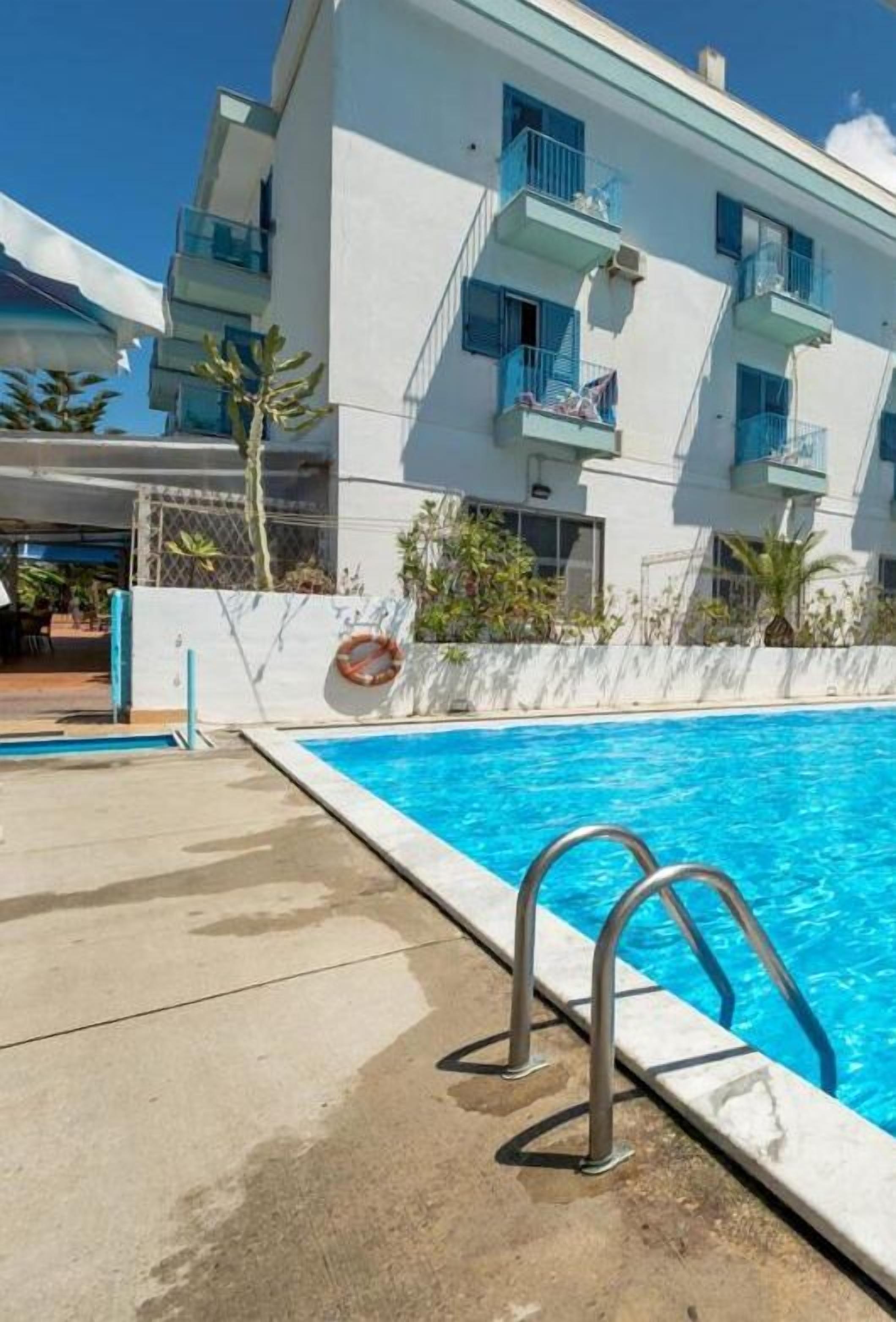 A modern building with balconies, a swimming pool, and a clear blue sky.