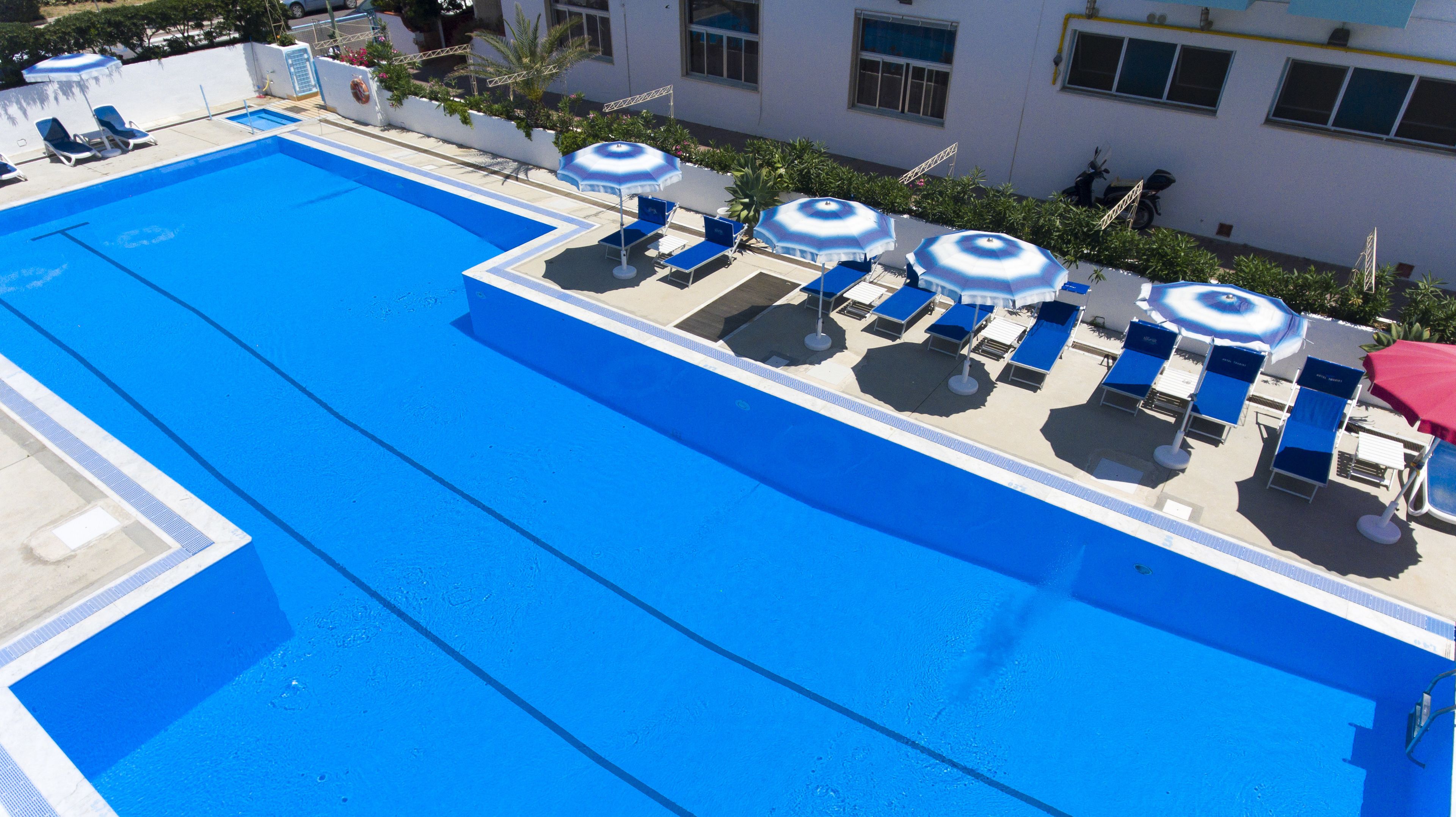 Une piscine sur le toit, avec de l’eau bleue, entourée de chaises longues et de parasols.