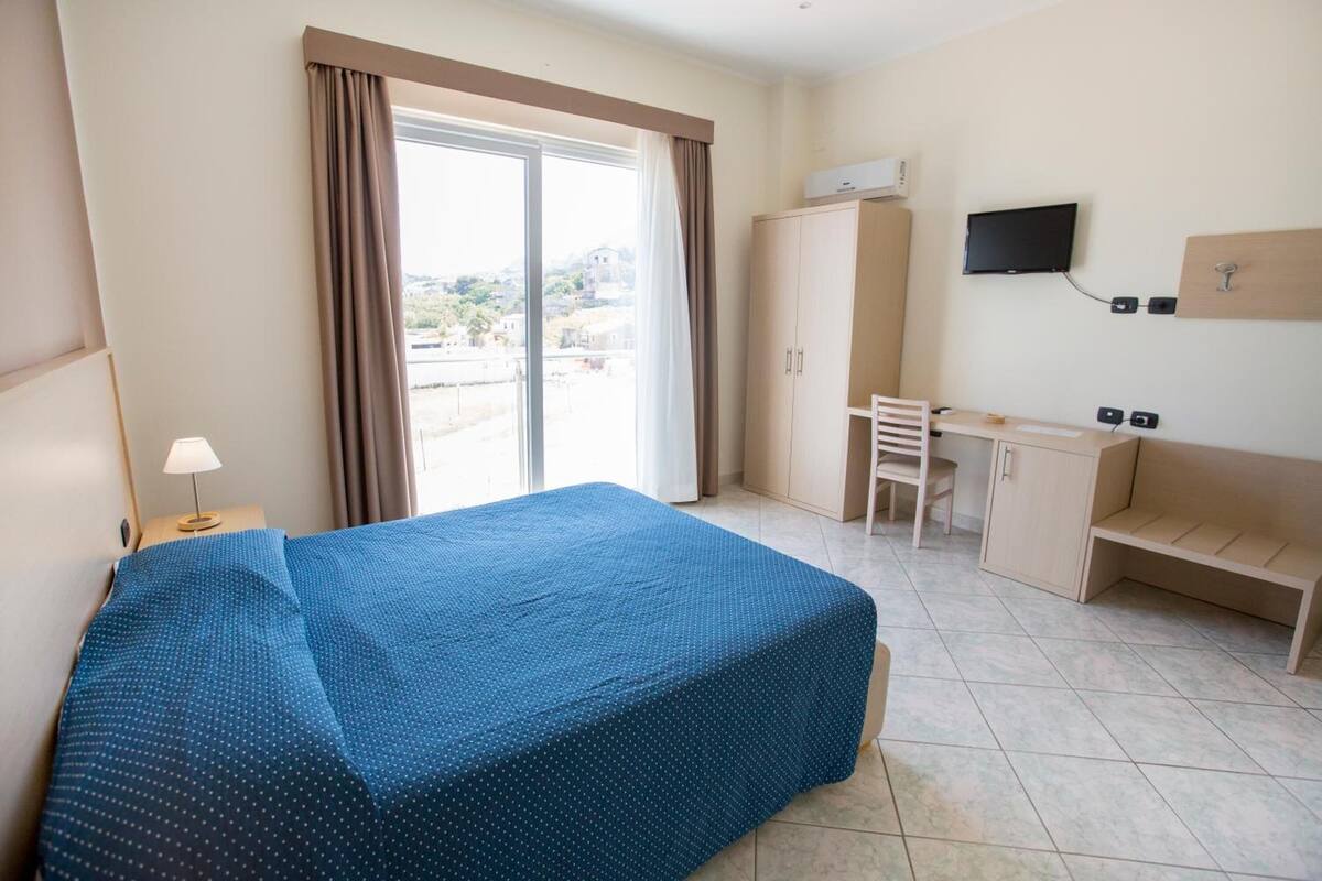 A hotel room with a bed, a desk, a chair, a TV, and a wardrobe.