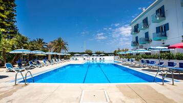 Piscina com espreguiçadeiras e guarda-sóis, cercada por palmeiras e um edifício com varandas.