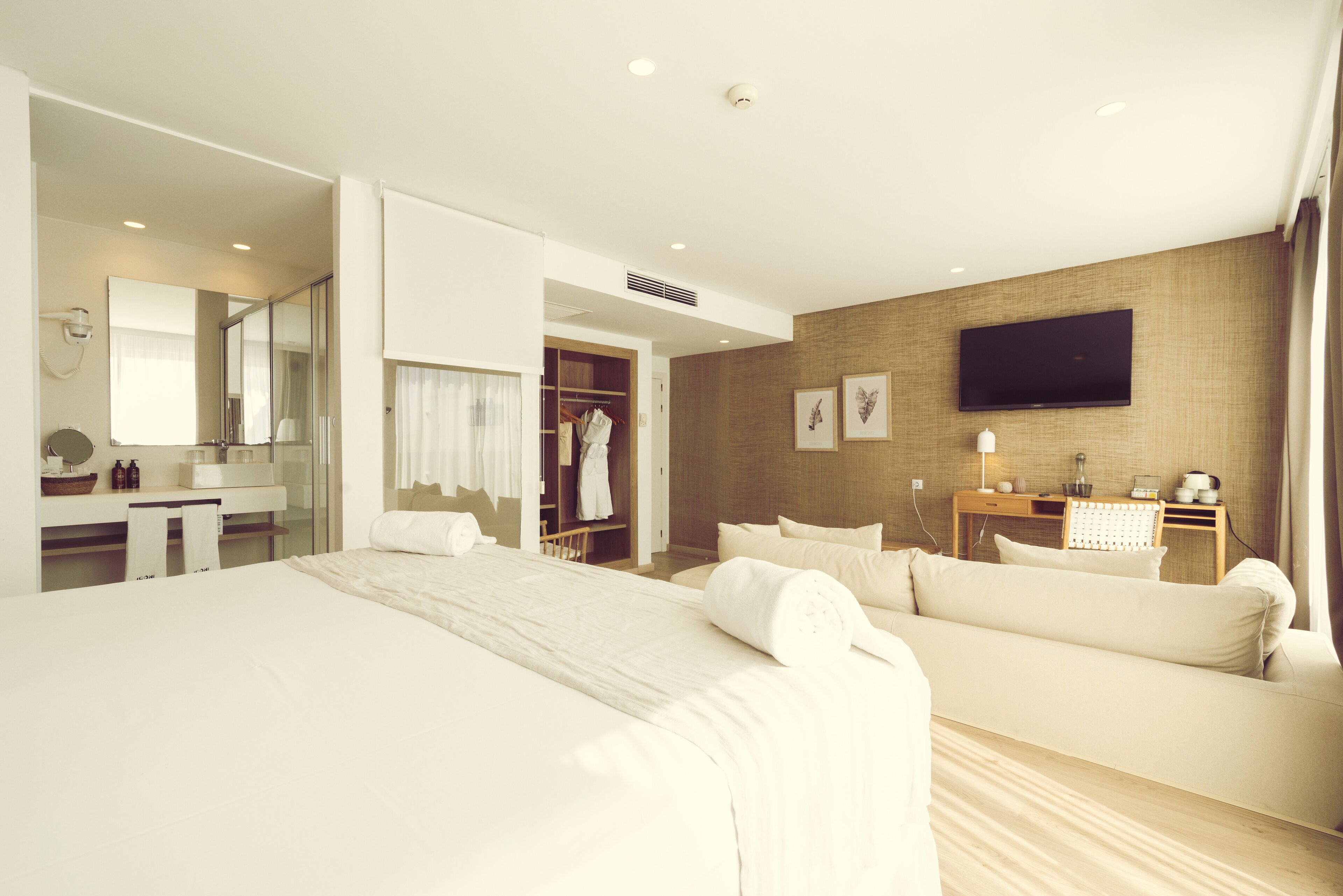 Habitación de hotel con una cama grande, un sofá, un televisor montado en la pared, un escritorio con espejo y un armario.
