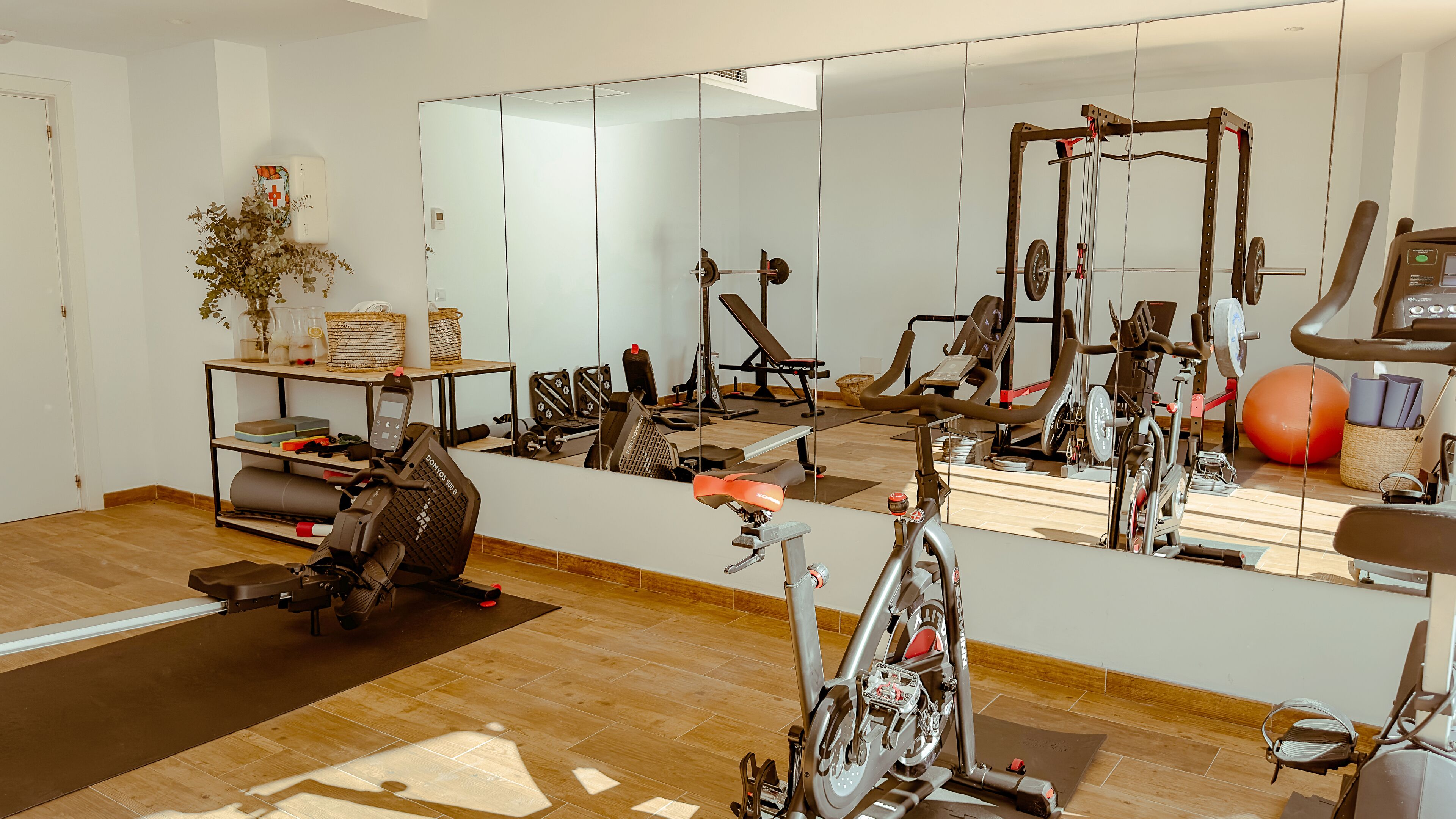Un gimnasio con equipo de ejercicio, un espejo grande y suelo de madera.