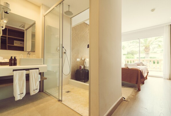 Un baño moderno con ducha de vidrio, un espejo grande y un lavamanos con artículos de aseo.