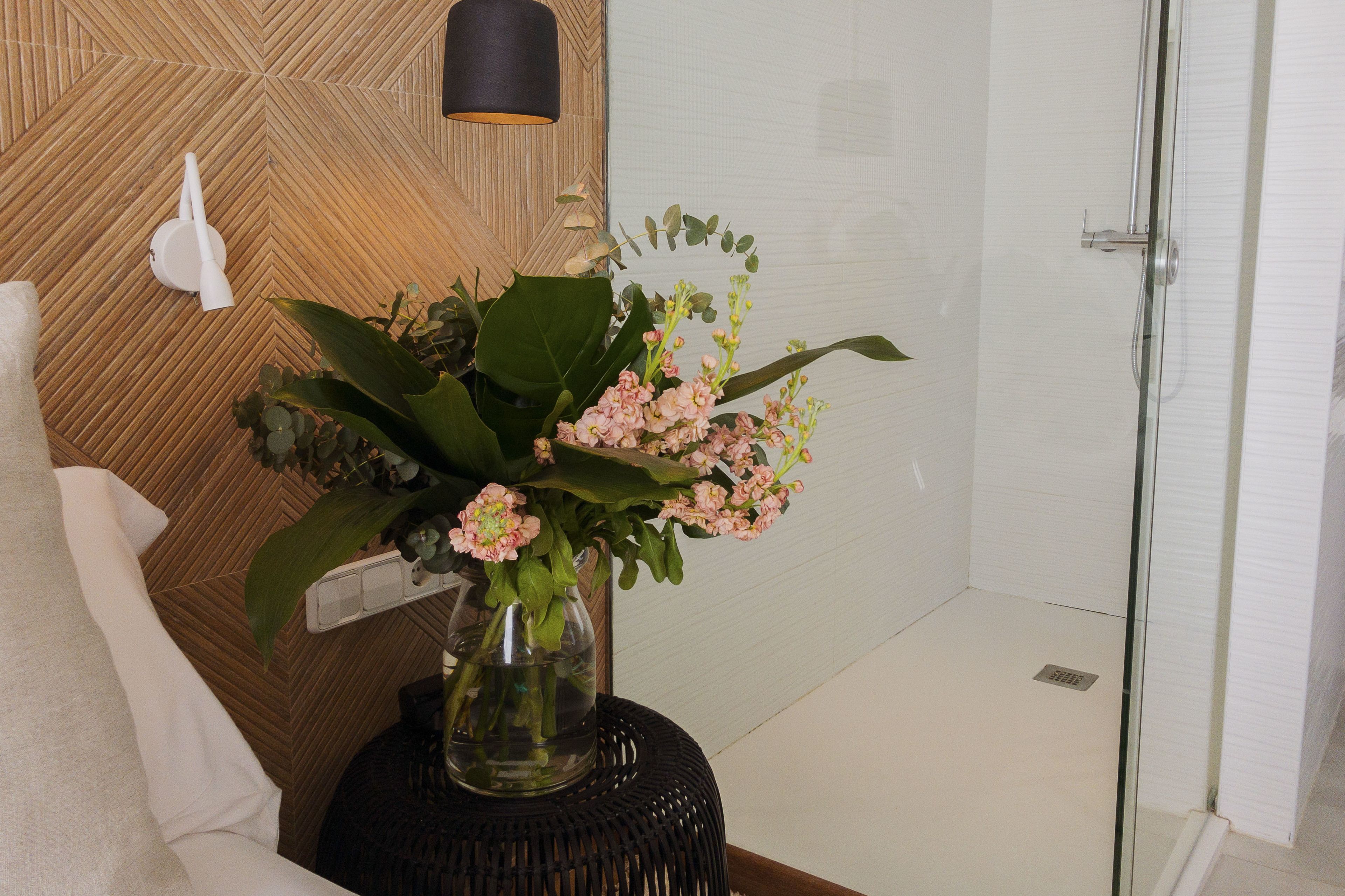 Un baño con ducha, una toalla blanca y un florero con flores sobre una mesa redonda negra.