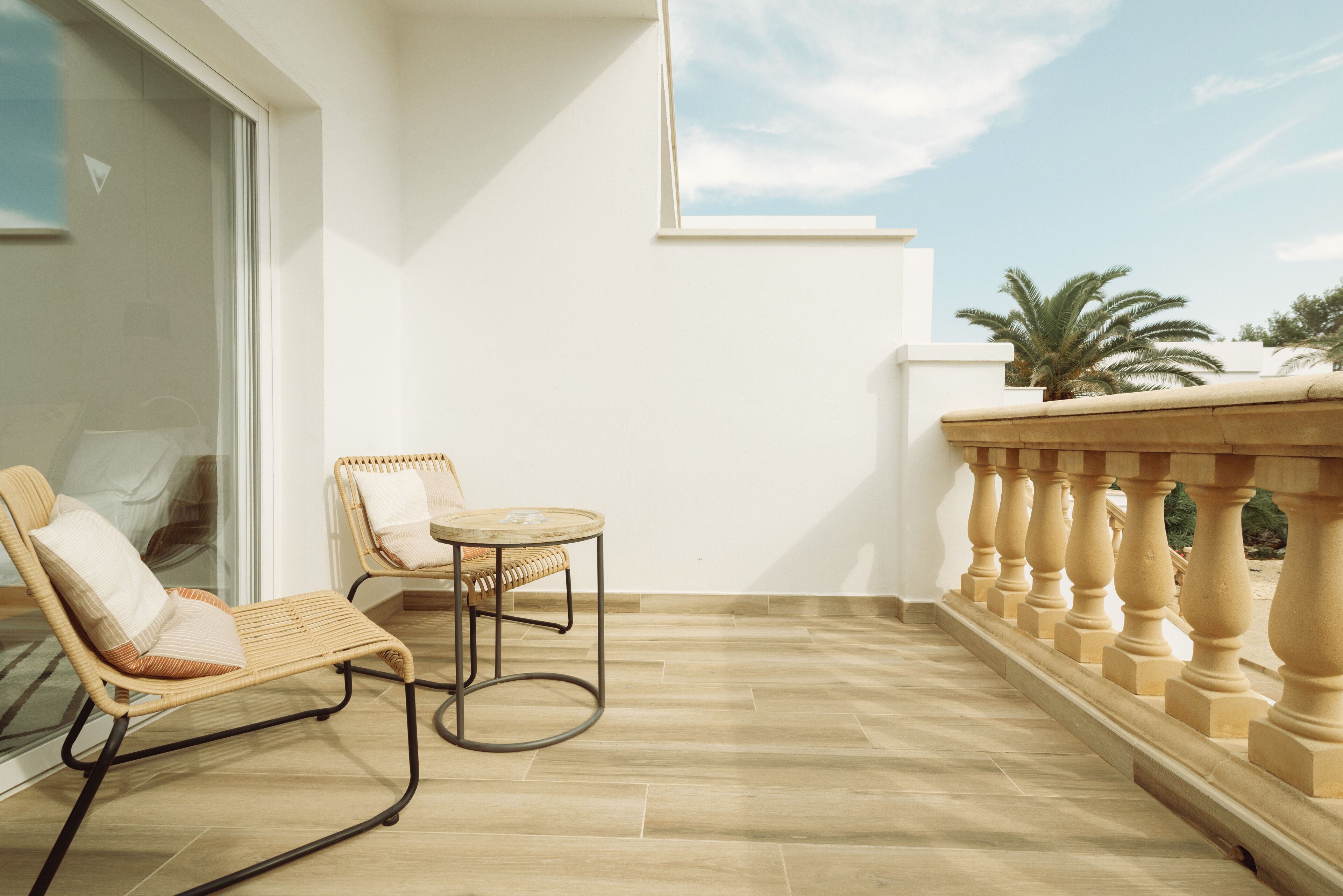 Un balcon avec deux fauteuils en osier, une petite table ronde et une balustrade.