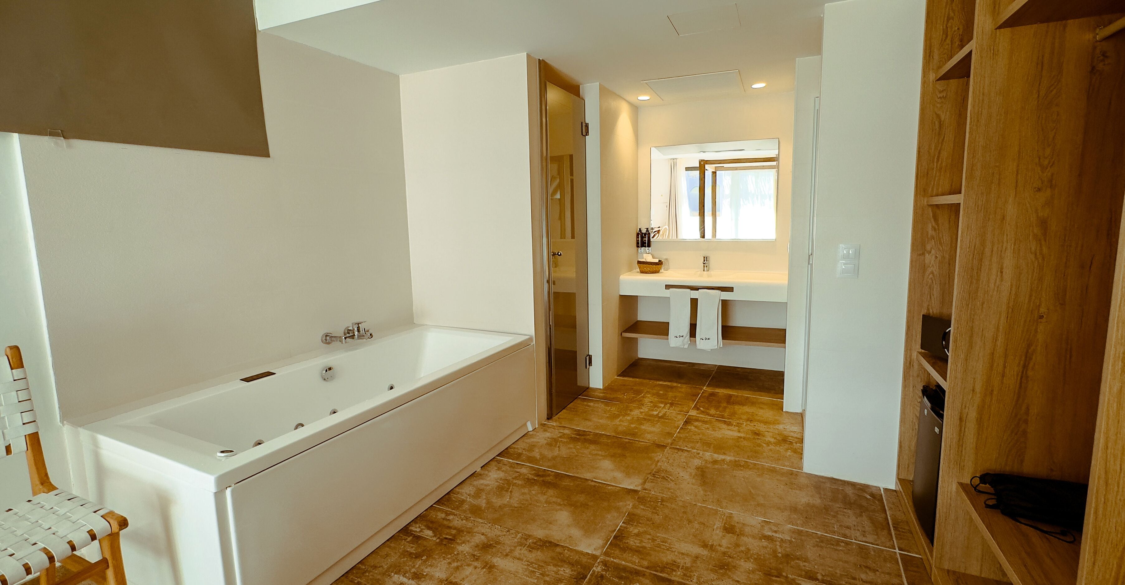 A modern bathroom with a large bathtub, a sink with a mirror, and a wooden cabinet.