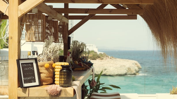 A wooden bar area with a chalkboard menu, wicker baskets, and a view of the sea. - ICON Valparaiso - Adults Only (Manacor)