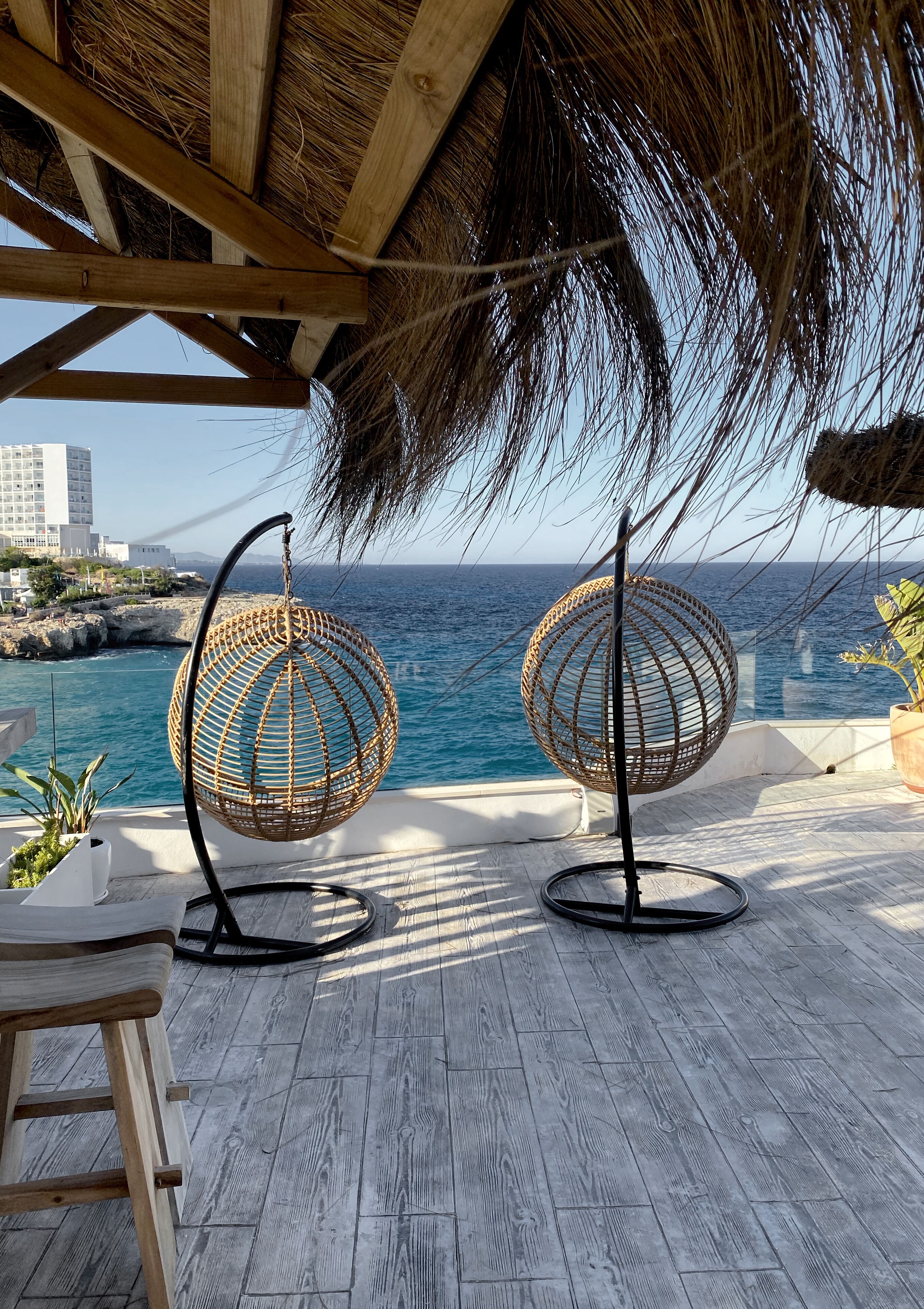 Terraza de madera con dos sillas colgantes de mimbre, con vista al mar.