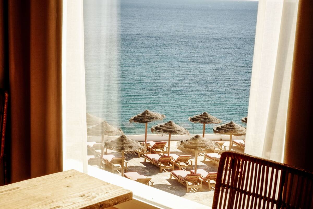 Une pièce avec vue sur la mer, comprenant une table et des chaises en bois, ainsi que plusieurs parasols en paille.