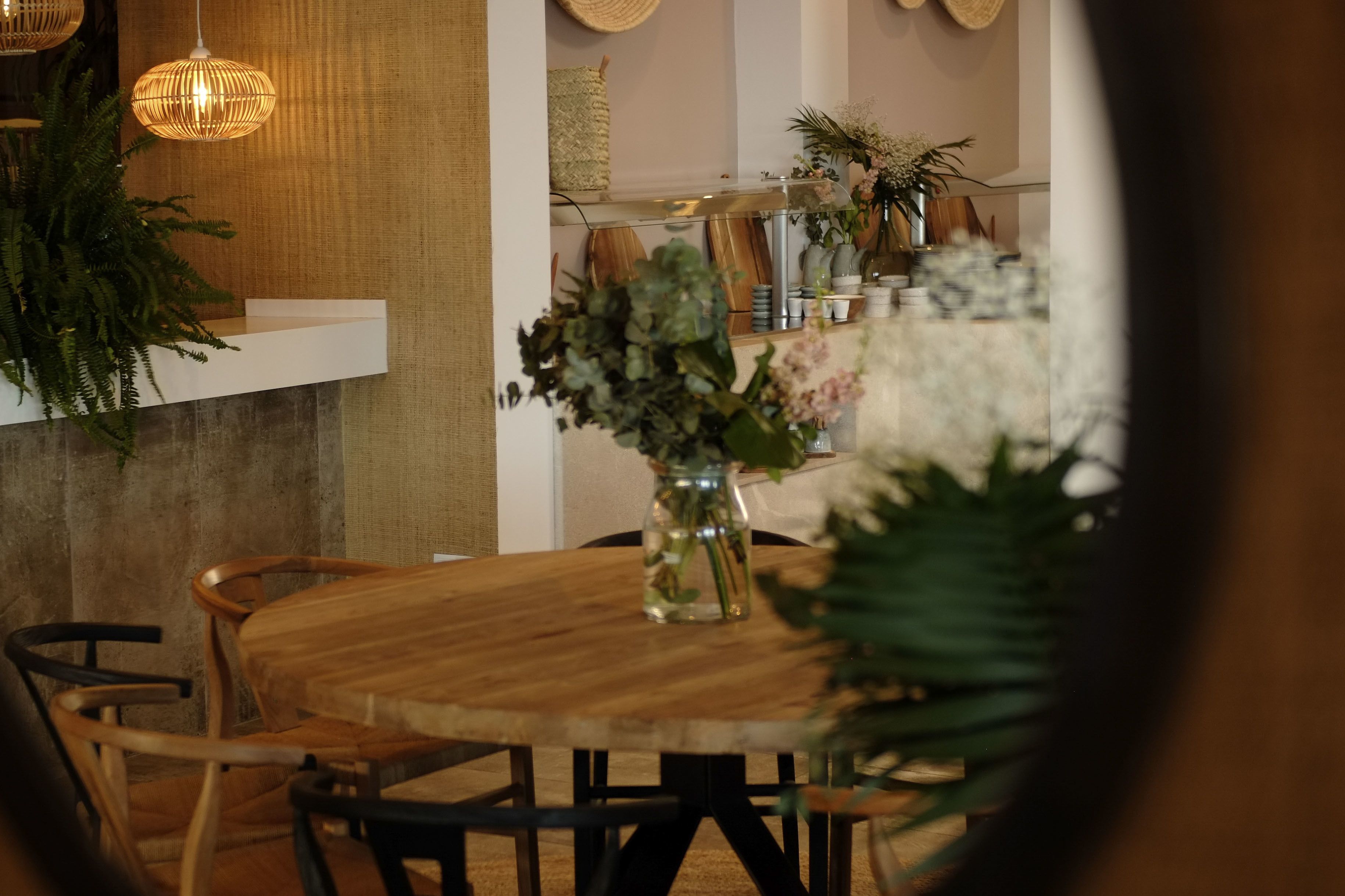 Una mesa de madera con sillas, un florero con flores y lámparas de mimbre colgantes.