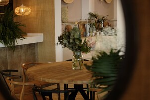 Una mesa de madera con sillas, un florero con flores y lámparas de mimbre colgantes.