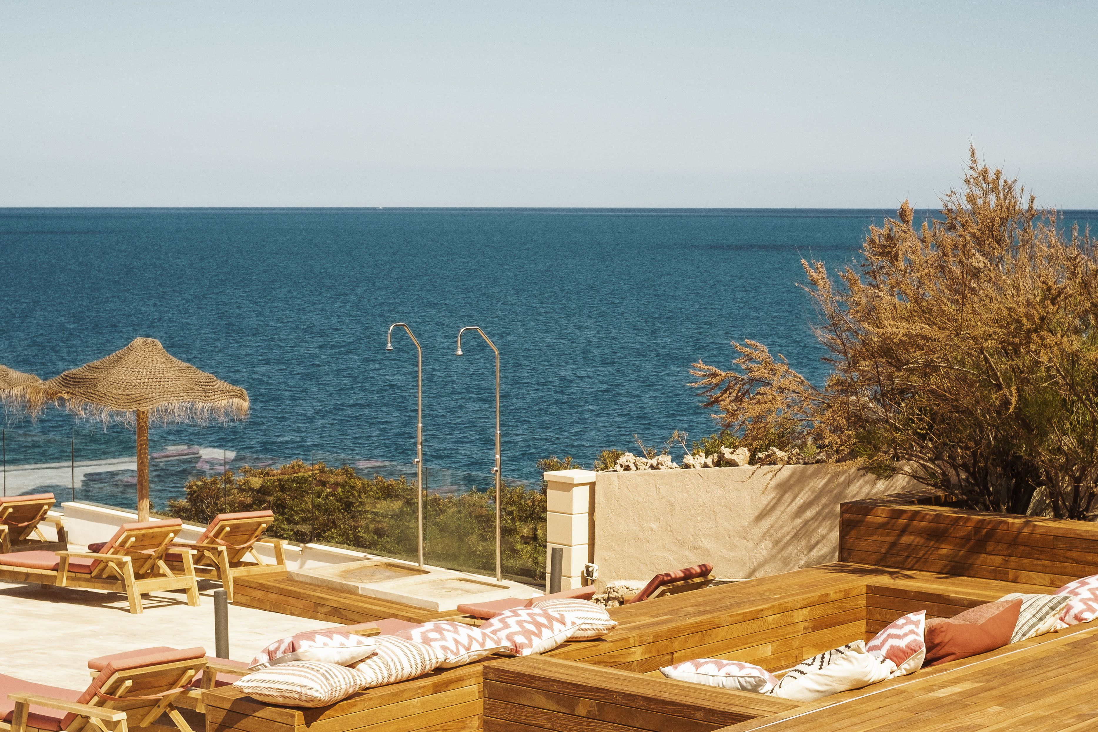 Una terraza de madera con sillones de descanso y un banco de madera con cojines, con vista a un cuerpo de agua.