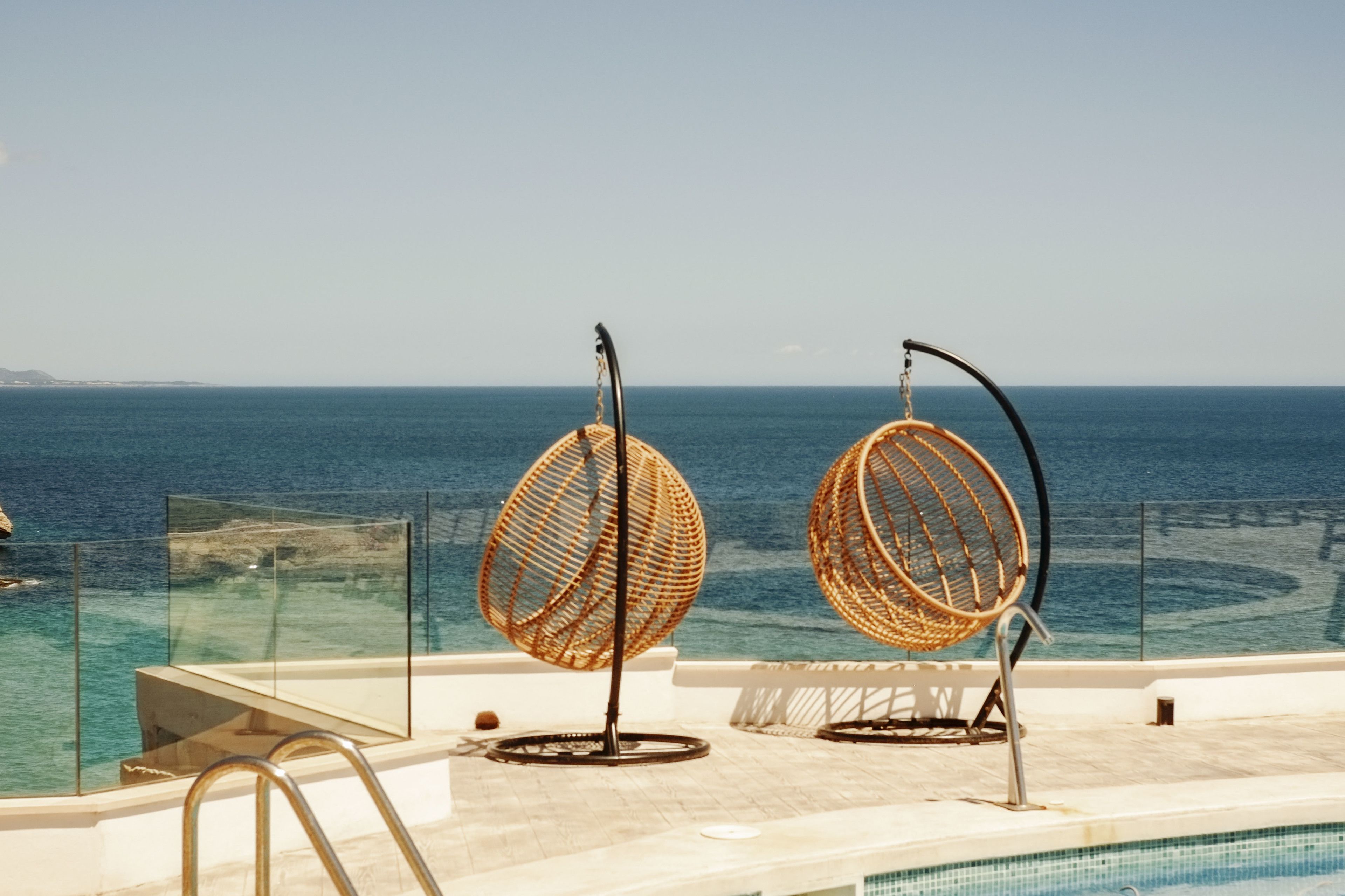 Ein Poolbereich mit zwei Korbstühlen und einer Glasbrüstung mit Blick auf das Meer.