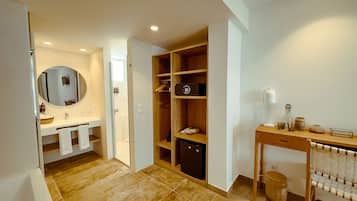 Un baño moderno con lavamanos, espejo y un vestidor con estantes y un refrigerador pequeño.