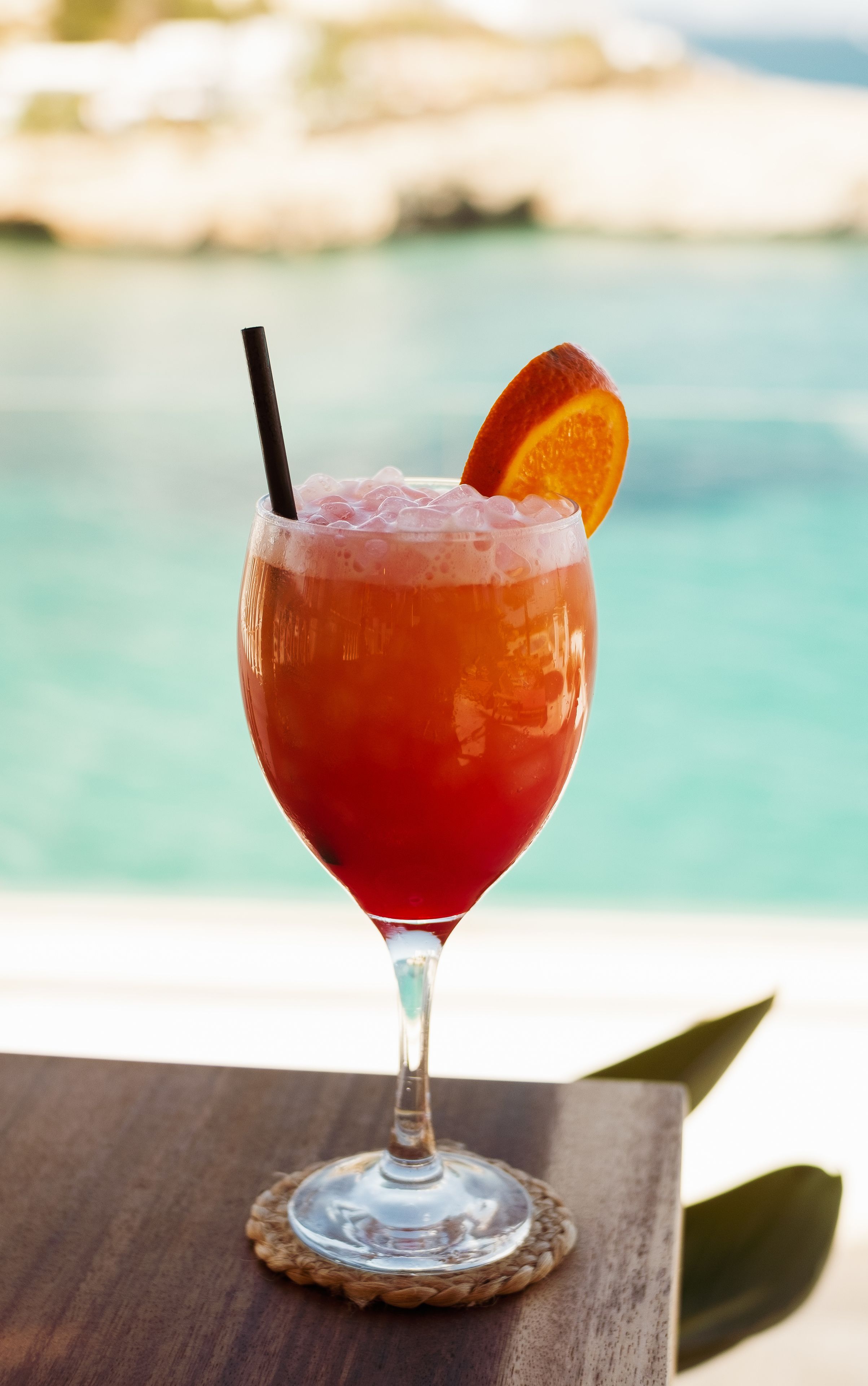 A cocktail in a stemmed glass with an orange garnish, placed on a wooden coaster.