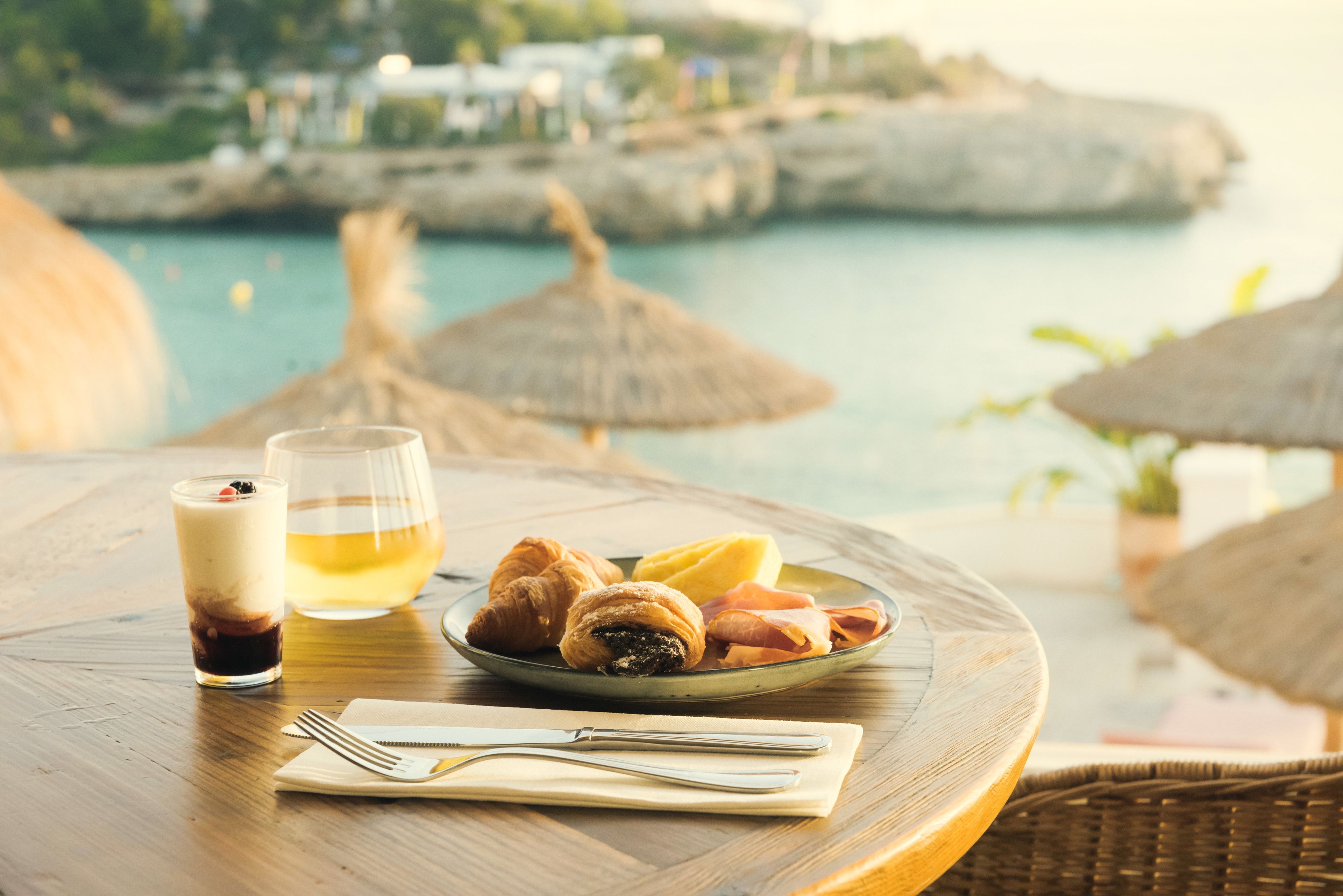 A table with a plate of food, a glass of drink, and a fork and napkin.