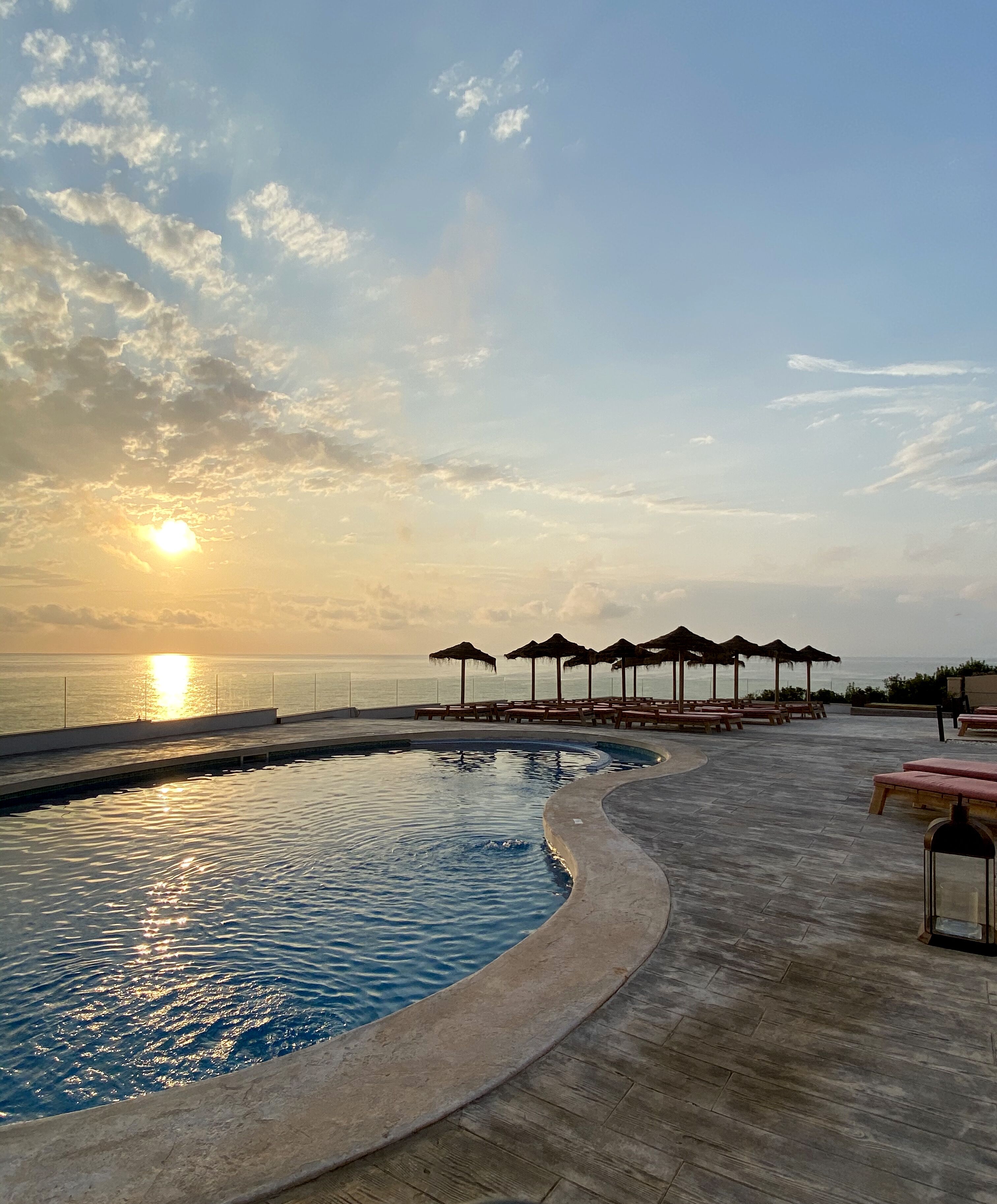 A pool area with a curved edge, lounge chairs, and umbrellas.
