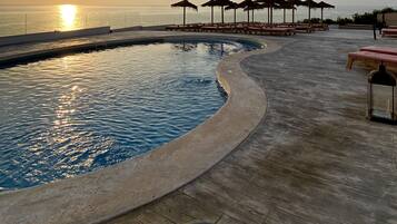A pool area with a curved edge, lounge chairs, and umbrellas.