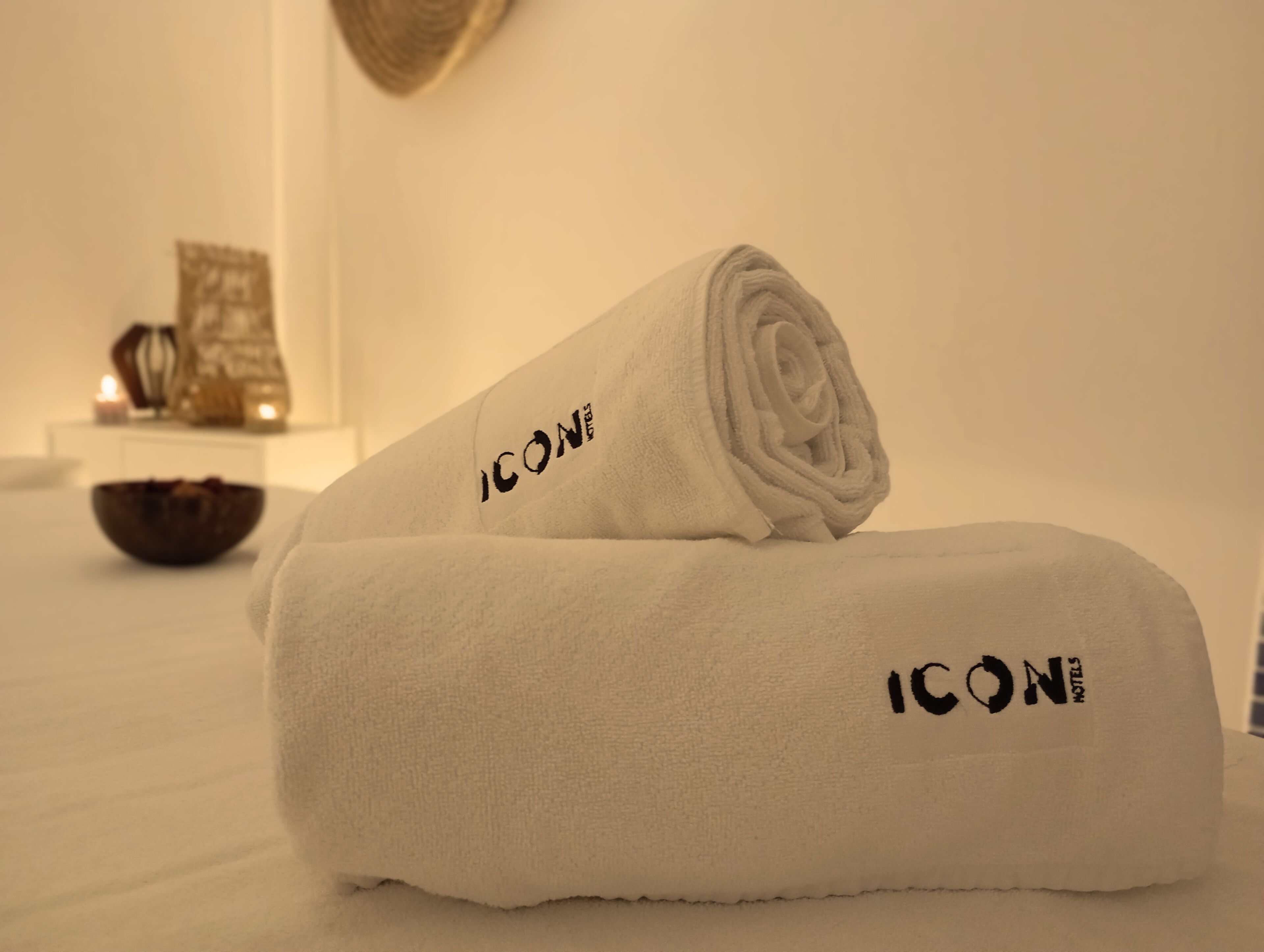 Toalha branca dobrada com o logotipo ICON sobre uma superfície branca, possivelmente em um quarto de hotel.