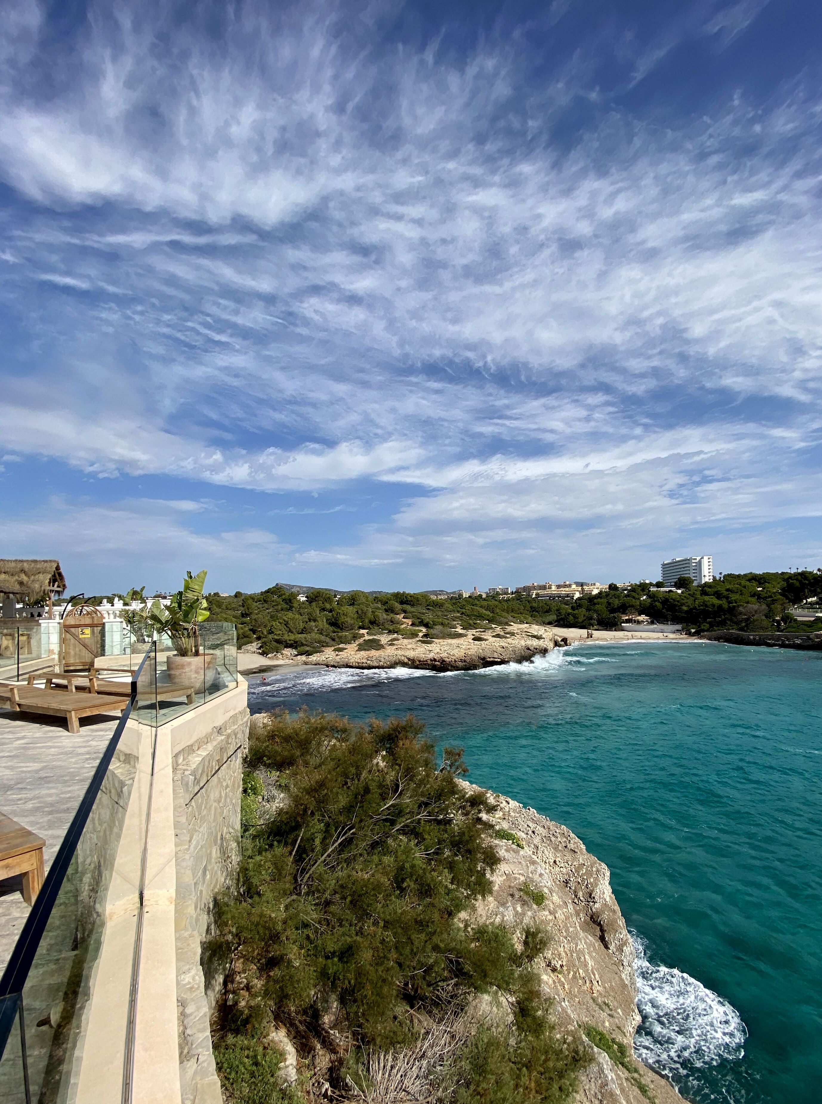 A coastal view with a clear sky, rocky shoreline, and a wooden deck overlooking the sea.