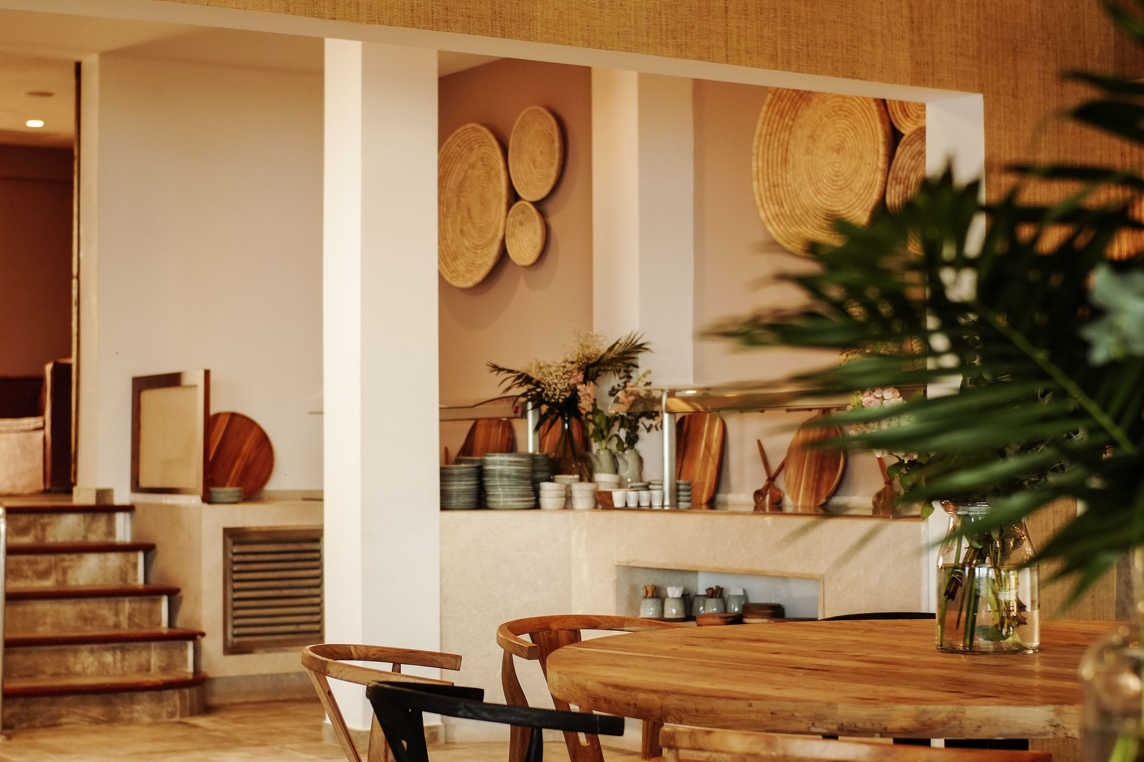 Ein Holztisch mit Stühlen, eine Vase mit Blumen und eine Wand mit gewebten Körben.