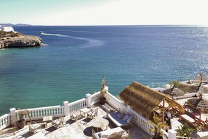 A seaside terrace with seating, a thatched-roof structure, and a view of the sea.