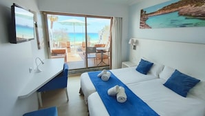 A hotel room with a bed, a desk, and a view of the beach through a sliding door. - Hotel Anba Romani (Sant Llorenc des Cardassar)