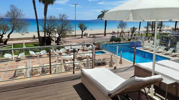 A poolside area with lounge chairs, a pool, and a view of the beach and ocean. - Hotel Anba Romani (Sant Llorenc des Cardassar)