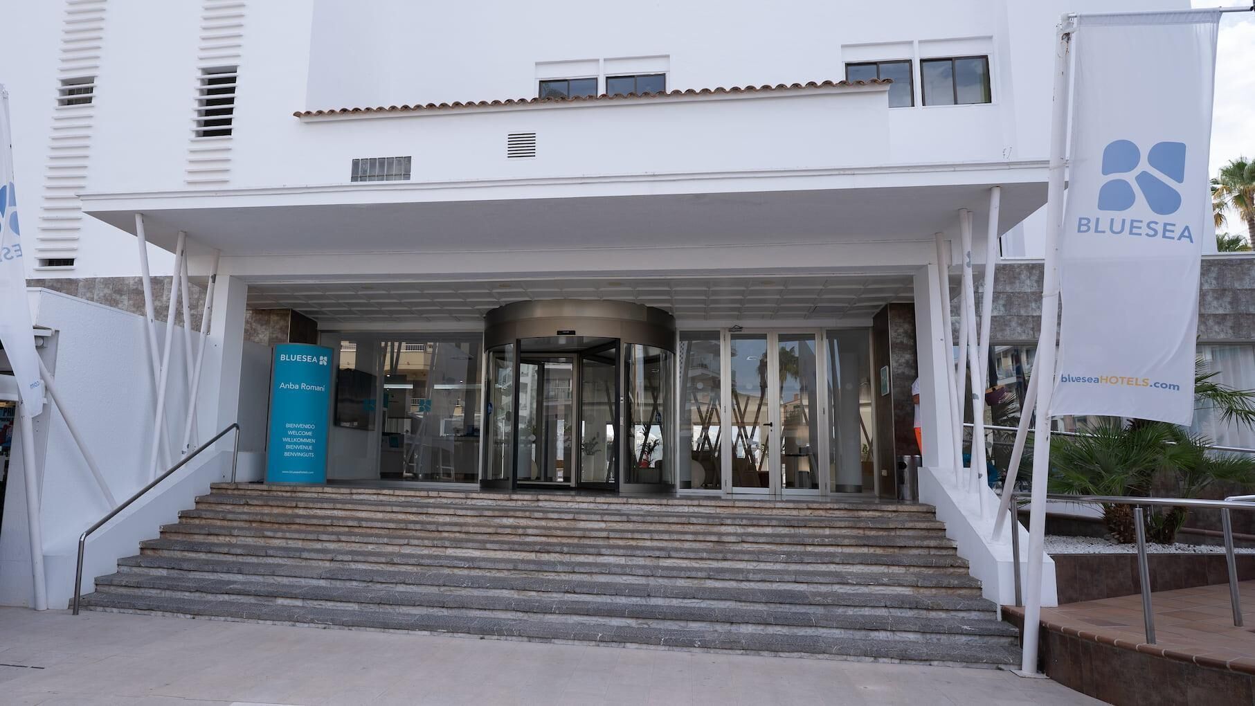A hotel entrance with a glass door, a blue sign, and a staircase leading up.