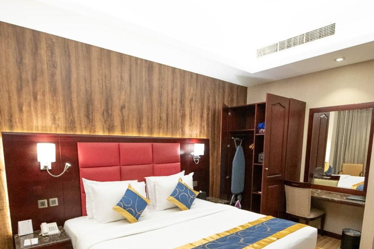A hotel room with a large bed, a wooden headboard, a bedside table with a phone, a wardrobe, and a mirror.