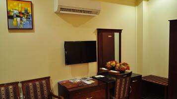 Habitación de hotel con escritorio, dos sillas, televisor de pantalla plana, aire acondicionado y un arreglo floral.