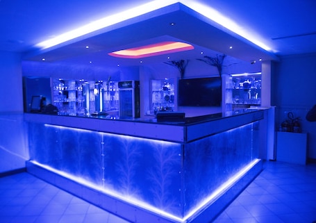 A modern bar area with a glass counter, ambient lighting, and a large screen.