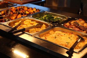 Un bufé con diversos platos, entre ellos verduras asadas, puré de papas y una cazuela.