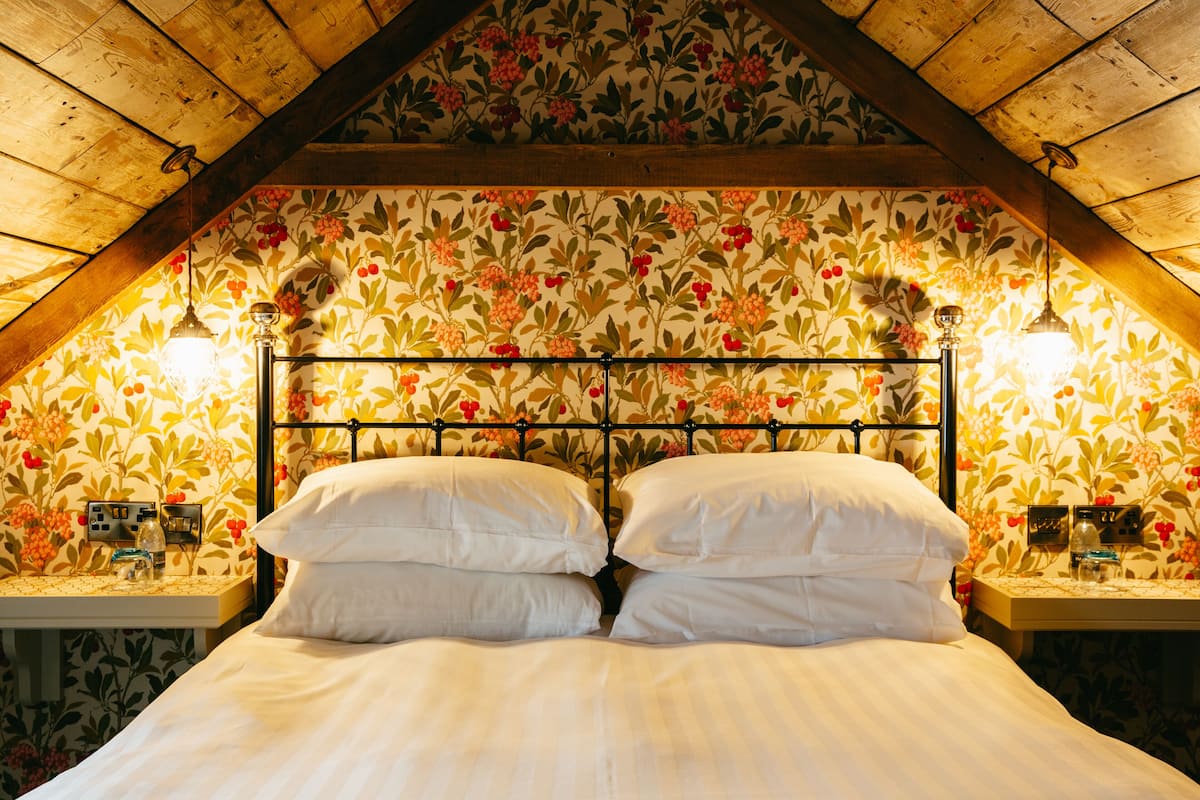 Een slaapkamer met een houten plafond, bloemenbehang, een metalen hoofdbord en bedlampjes.