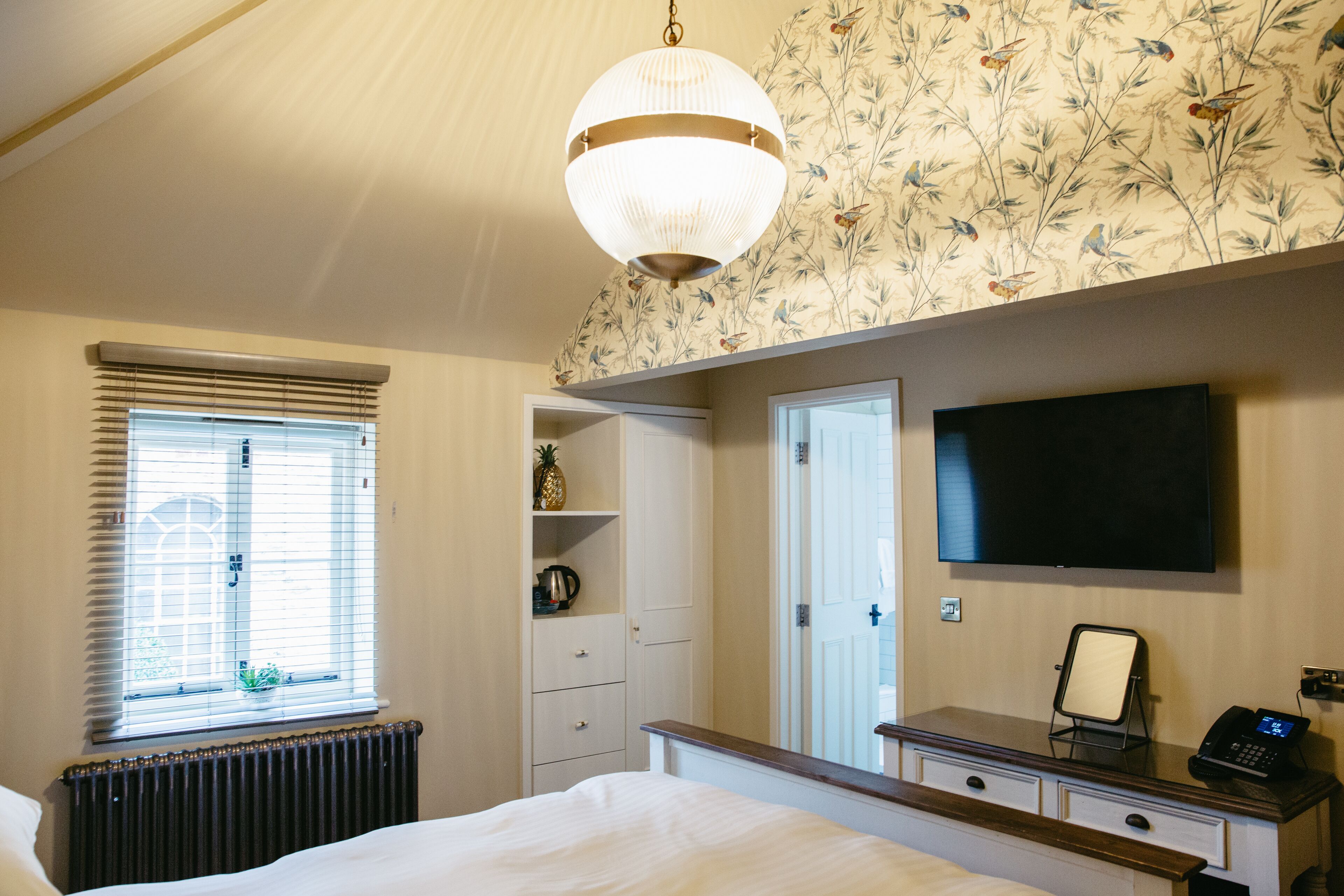 Ein Schlafzimmer mit einem Bett, einem Schminktisch, einem Spiegel, einem Fernseher und einem Fenster mit Jalousien.