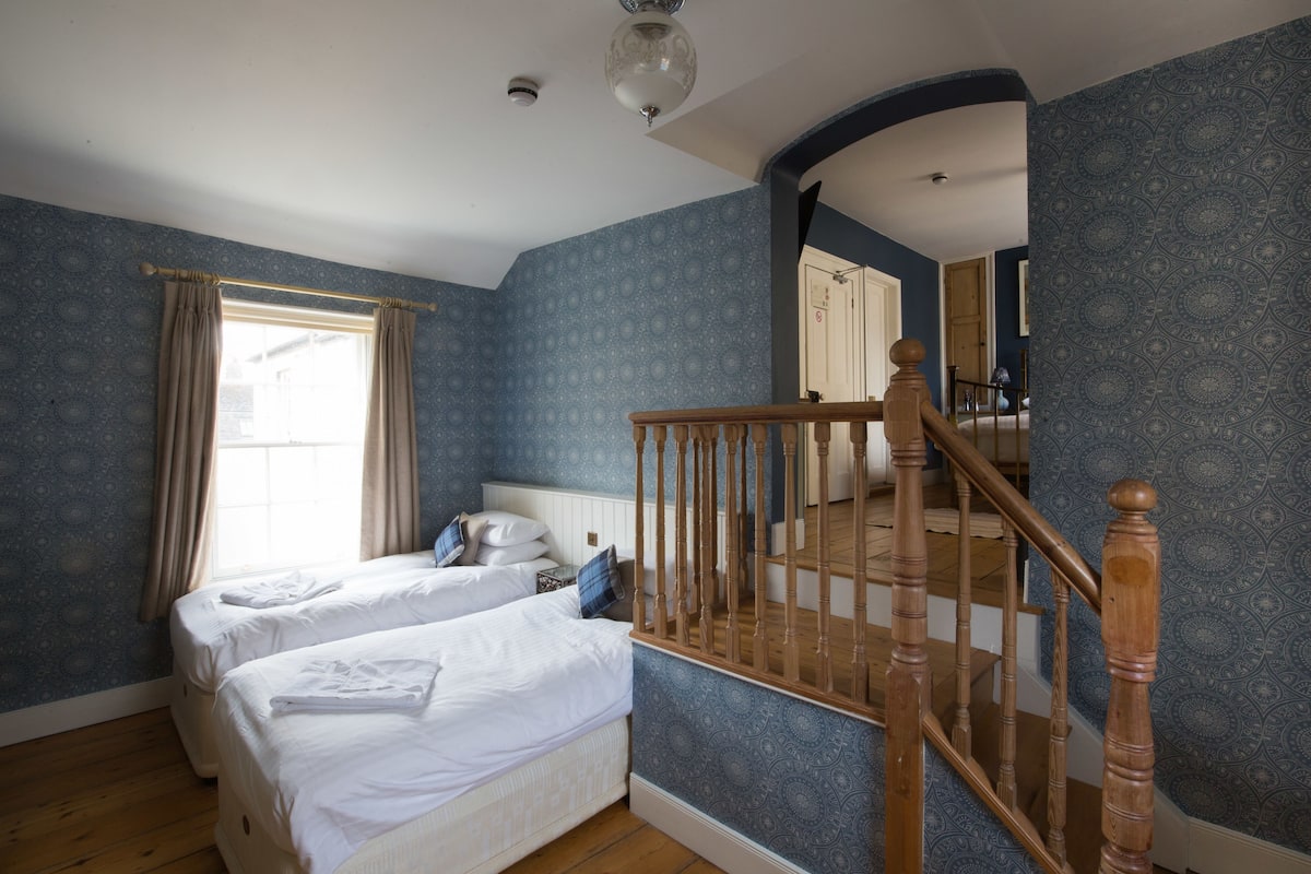 Een slaapkamer met twee bedden, een houten trap en een groot raam met gordijnen.