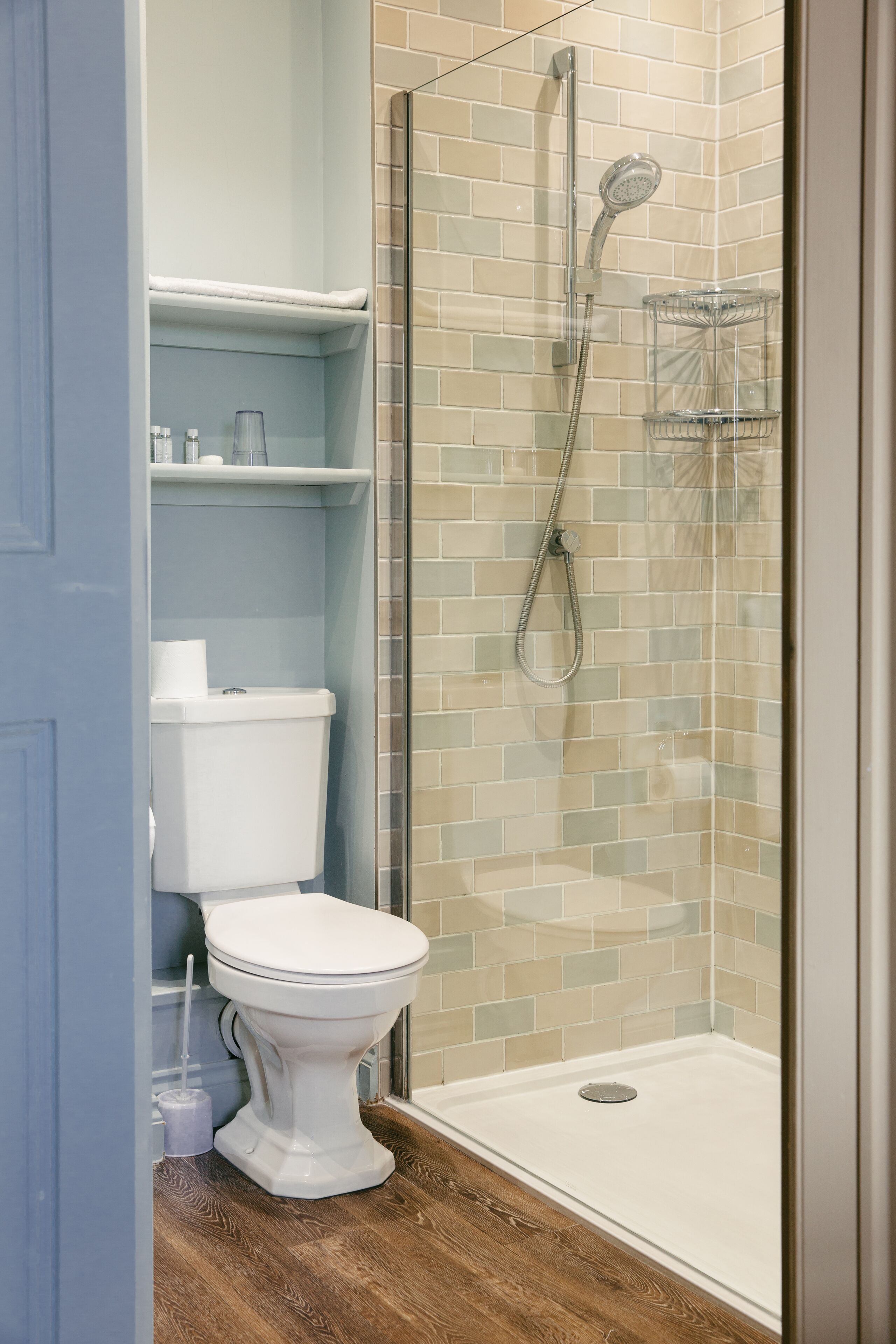 Een badkamer met een wit toilet, een douche met glazen wanden en een houten vloer.