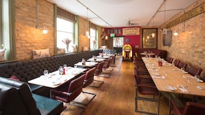 A restaurant with a long wooden table and booths, brick walls, and a vintage jukebox. - Crown Hotel Stamford (Stamford)