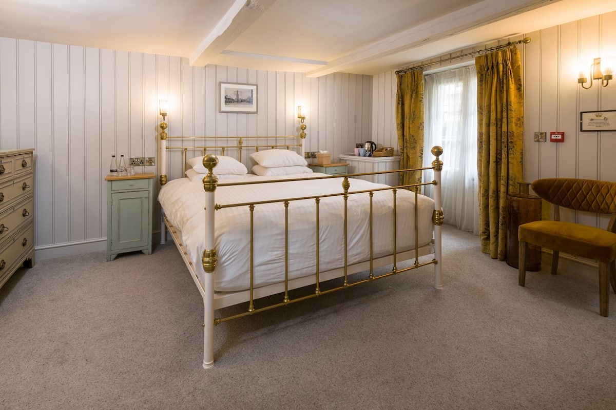 Een slaapkamer met een hemelbed, nachtkastje, dressoir en stoel.