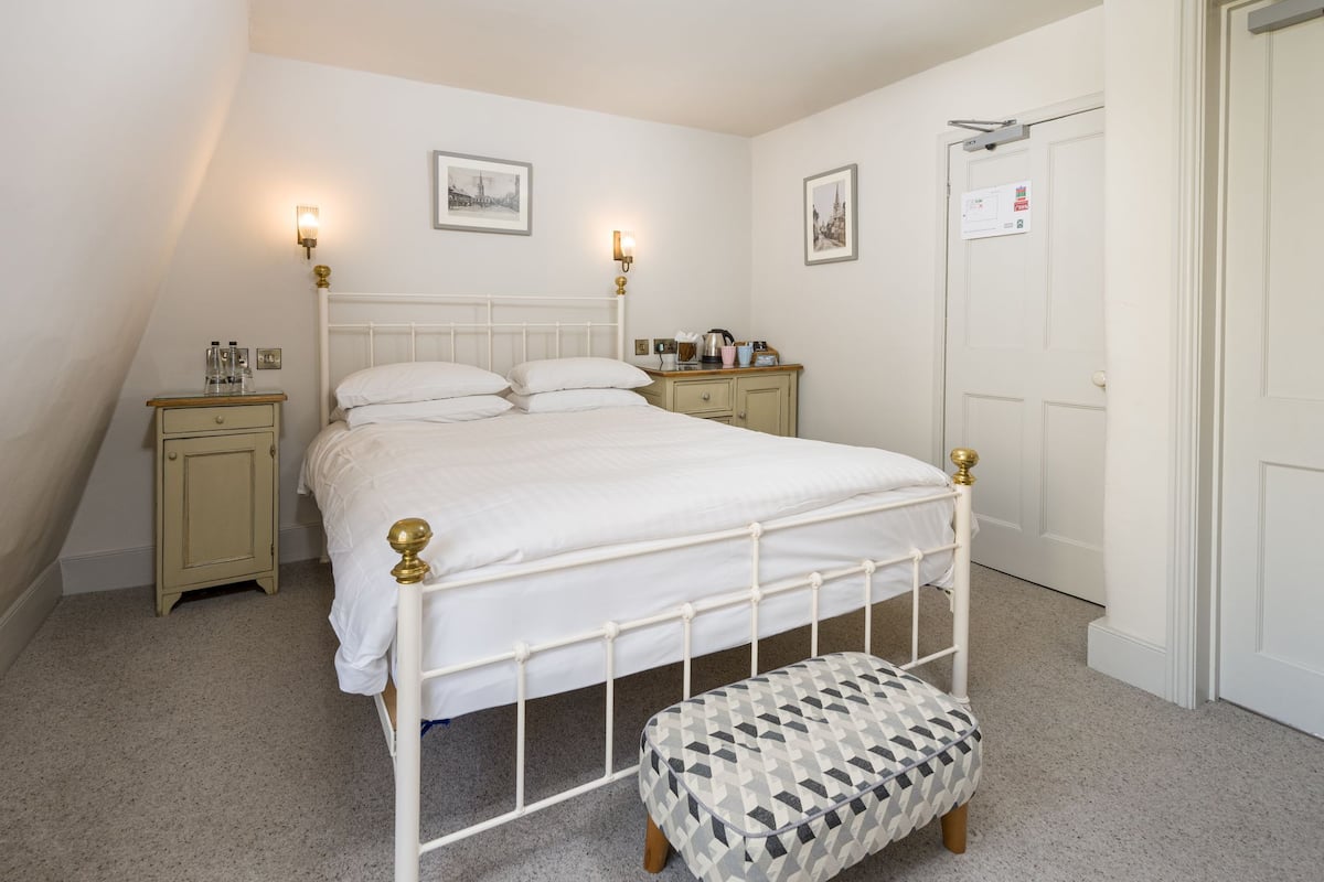 Een slaapkamer met een wit bed, twee nachtkastjes, een bankje en twee wandlampen.