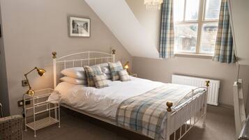 A neatly arranged bedroom with a bed, bedside lamps, a radiator, and a window with curtains.